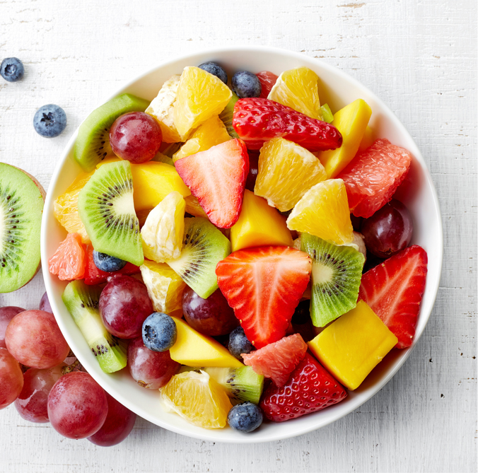 A bowl of salad made from foods such as bananas, strawberries, raspberries, blueberries, mini pancakes, etc